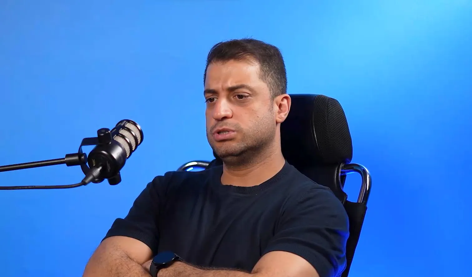 A man speaks into a studio microphone against a blue background.