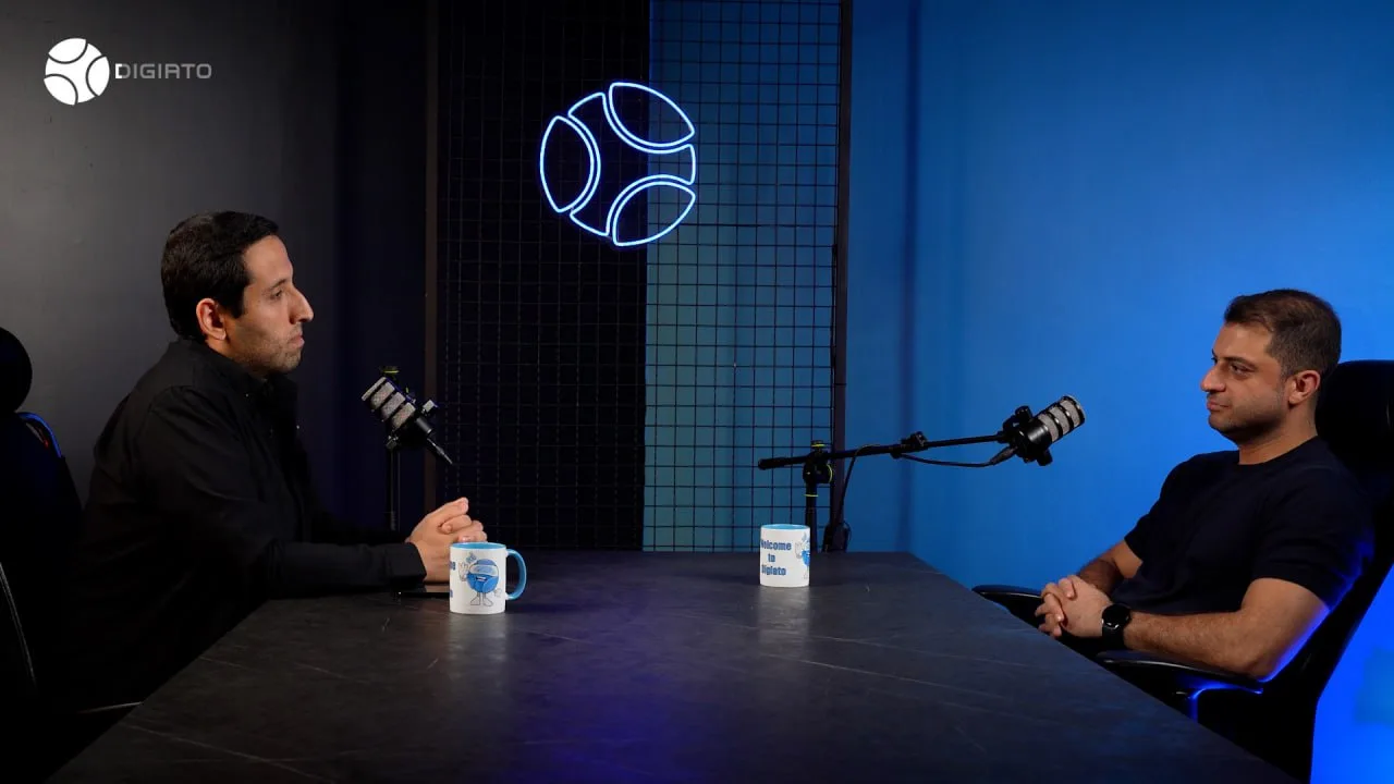 Two men sit across a table with microphones in Digiato’s studio.