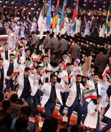 Group in light jackets waving Iranian flags along an arena walkway.