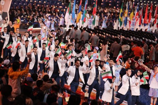 Group in light jackets waving Iranian flags along an arena walkway.