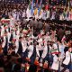 Group in light jackets waving Iranian flags along an arena walkway.