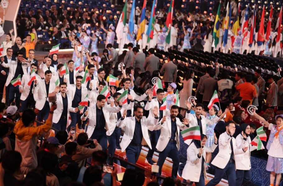 Group in light jackets waving Iranian flags along an arena walkway.