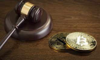 A judge’s gavel beside two physical Bitcoin tokens.