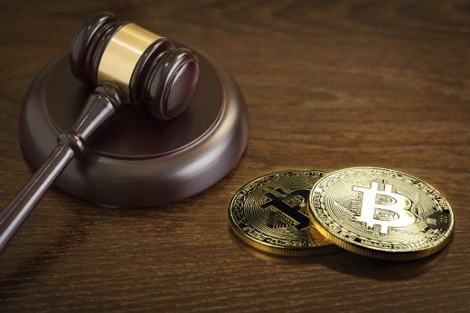 A judge’s gavel beside two physical Bitcoin tokens.