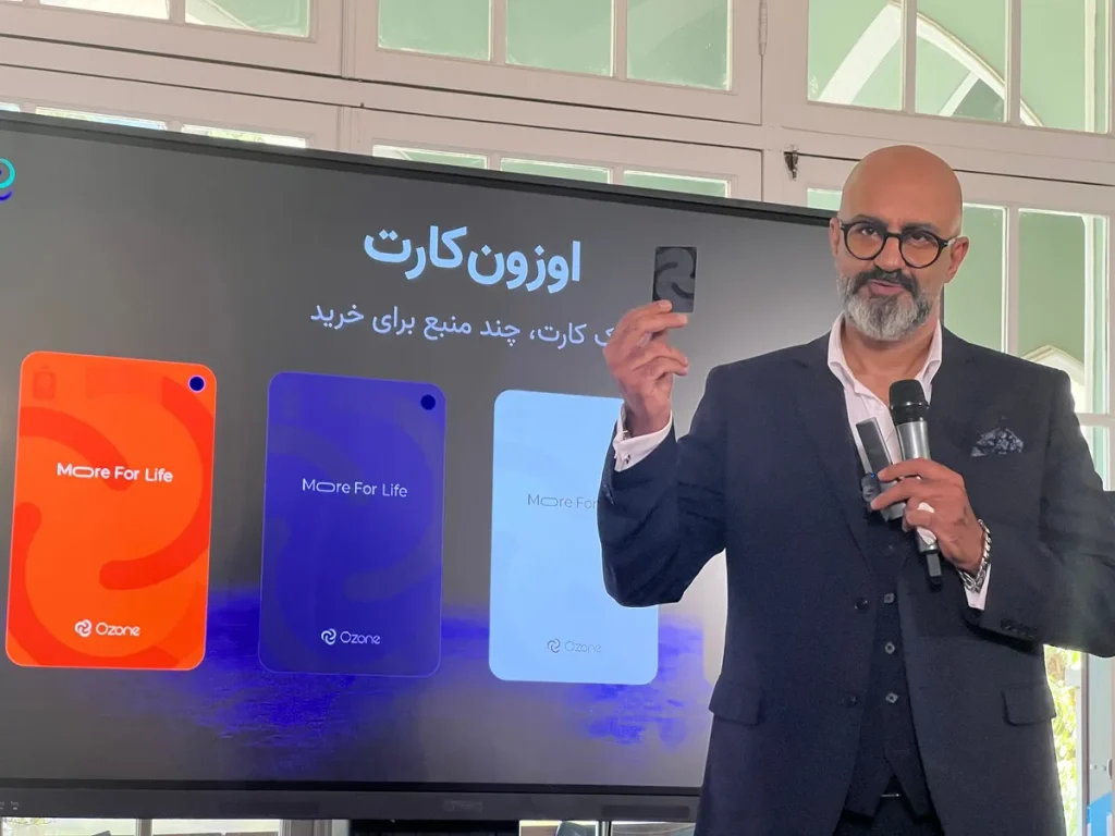 Sohail Haghighat holds a card beside a display showing Ozone Card designs.