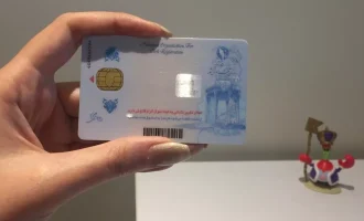 A hand holding an Iranian national ID card with an embedded chip.