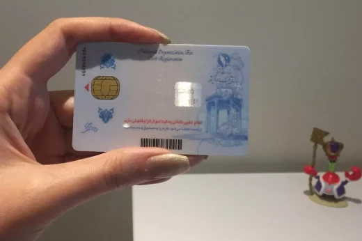 A hand holding an Iranian national ID card with an embedded chip.