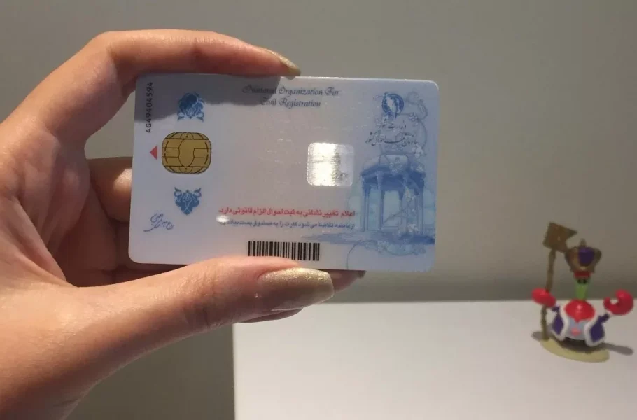 A hand holding an Iranian national ID card with an embedded chip.