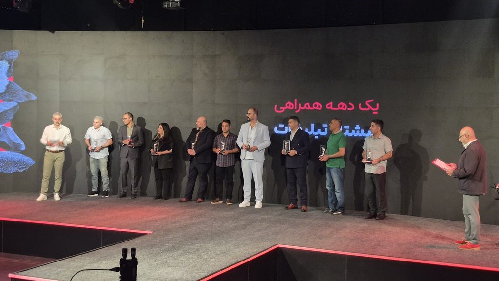 A group of participants stand onstage holding awards at Digikala’s marketplace anniversary event.