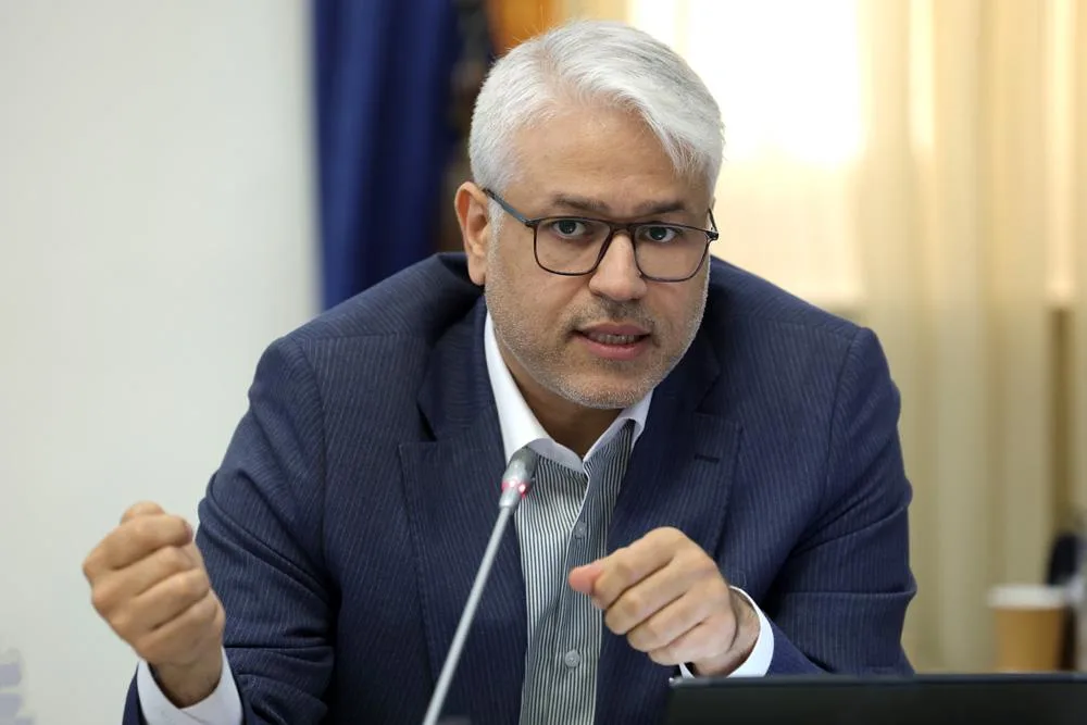 Ehsan Chitsaz, wearing glasses and a dark suit, speaks into a desk microphone.