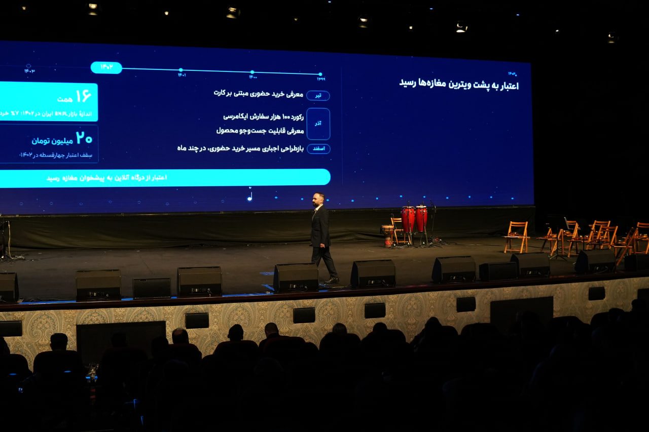 A speaker and a large blue presentation screen facing the audience.