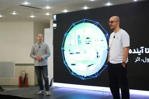 Two people stand on a stage in front of a large presentation screen.
